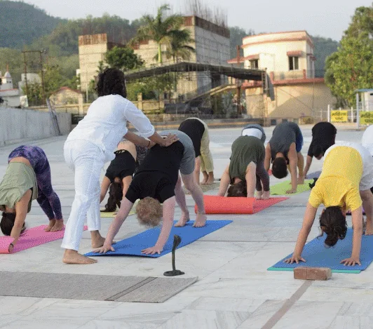 Teacher guiding students in downward dog on yoga mats on the ghat