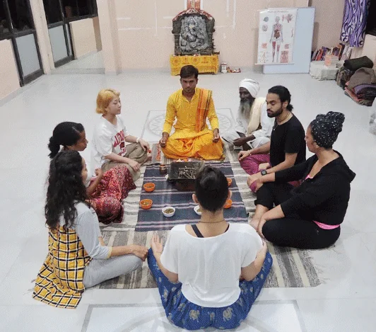 Teacher leading a ceremony with students seated on the floor at Avatar Yoga School