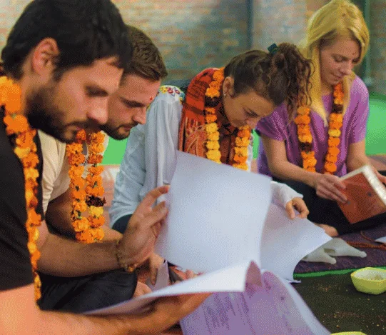 Students wearing garlands and reading course notes during yoga teacher training